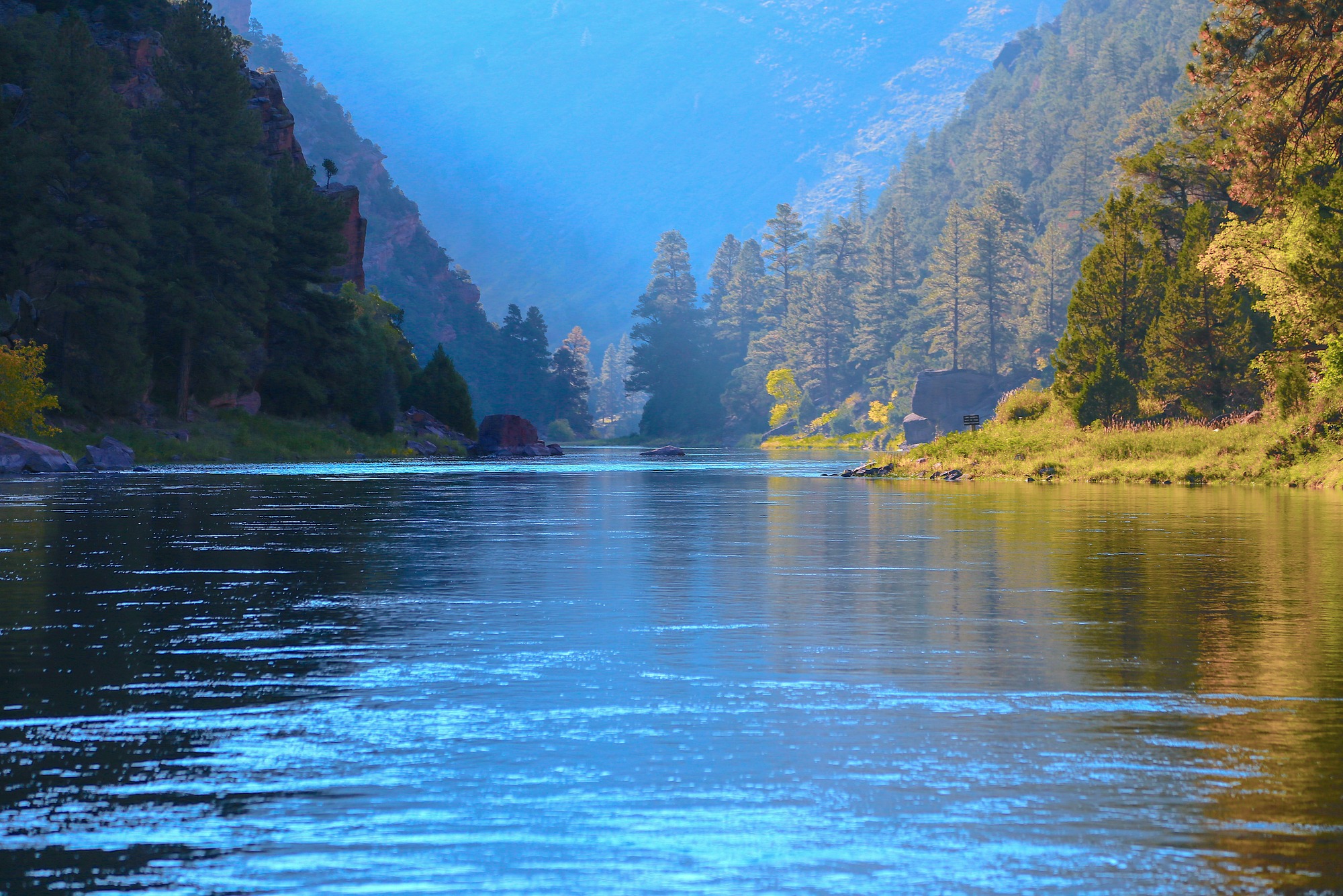 Serene river winding through lush, tree-covered mountains, bathed in soft blue light; highlights the tranquility of nature and outdoor beauty.