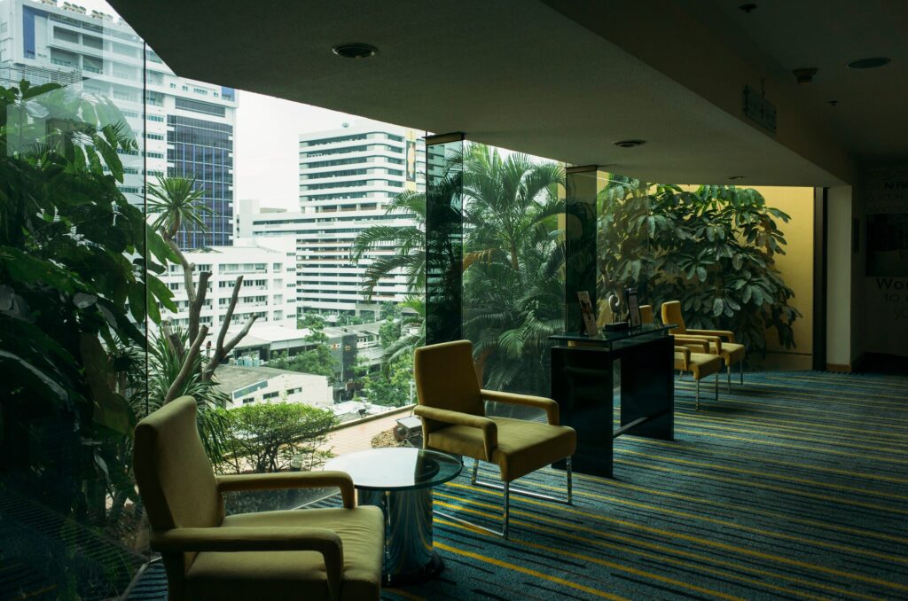 Modern lounge featuring yellow chairs and a glass wall overlooking a cityscape with greenery. Ideal space for relaxation or meetings.